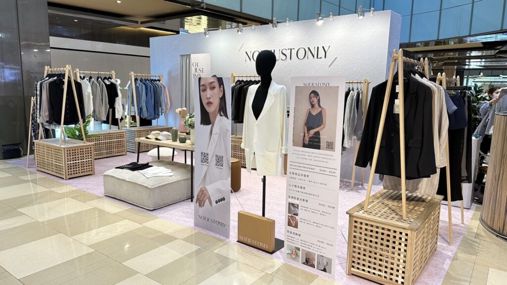 服飾品牌快閃展場全景，多支小白鷺衣架架在木格柵置物櫃上，掛滿當季服裝