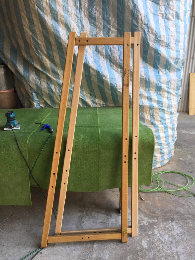 整新前的舊梯型框架立在工作台旁，木色變深、留著出攤的痕跡