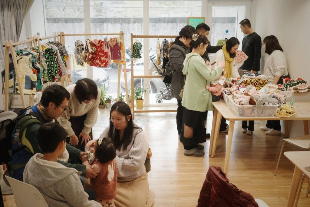 快閃店裡客人帶著孩子在挑童裝，窗前的木衣架掛著小件衣物